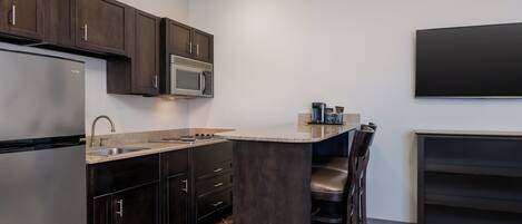 A modern kitchen with dark wood cabinets, a stainless steel refrigerator, a microwave, and a built-in island with bar stools.