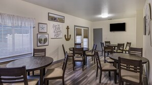 Un espace repas avec des tables et des chaises rondes, un téléviseur à écran plat et un mur orné de tableaux et d’une ancre décorative.