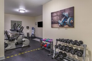 A gym with exercise equipment, a wall-mounted TV, and a rack of dumbbells. - Stay-Over Suites (Hopewell)