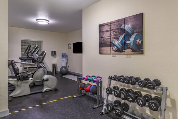 A gym with exercise equipment, a wall-mounted TV, and a rack of dumbbells.