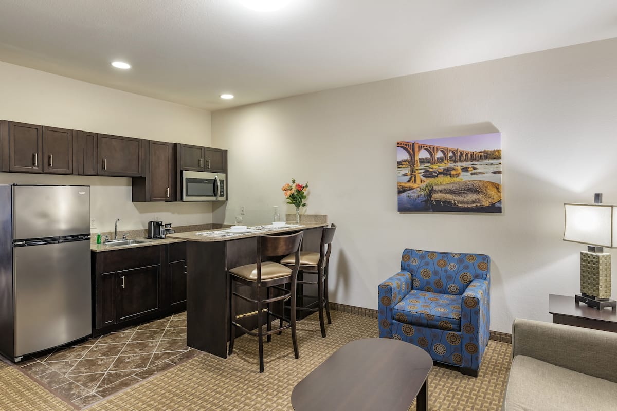 A compact kitchen with dark cabinets, a stainless steel refrigerator, a microwave, and a small island with bar stools.