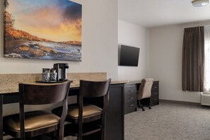 A hotel room with a desk, two chairs, a coffee machine, a flat-screen TV, and a window with curtains. - Stay-Over Suites (Hopewell)