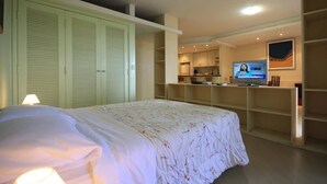 A bedroom with a bed, a TV, and a kitchenette area. - Lucio Costa 103 (Rio de Janeiro)