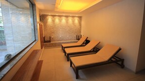 A spa room with three sun loungers, a stone wall, and a glass window. - Lucio Costa 103 (Rio de Janeiro)