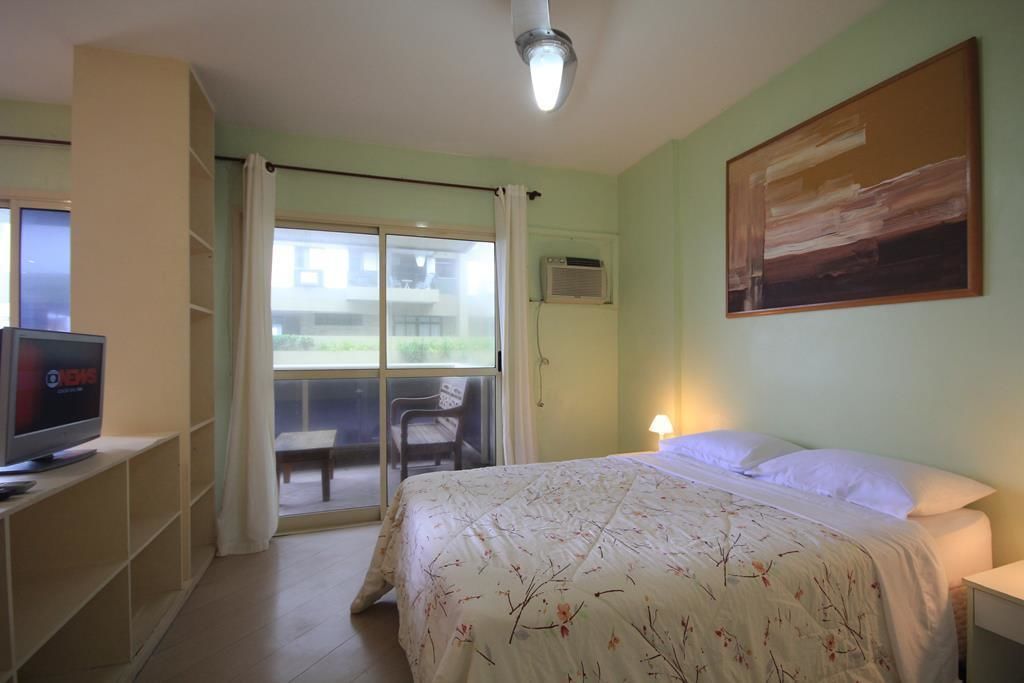 Een slaapkamer met een bed, een televisie, een schuifdeur naar een balkon en een schilderij aan de muur.