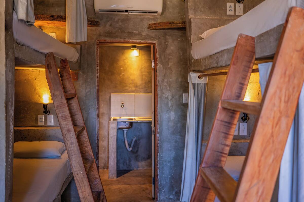 Ein schmaler Flur mit einer Holzleiter, einem Waschbecken und einer Tür zu einem kleinen Badezimmer.