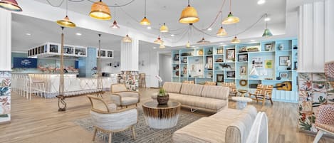 Ein geräumiger Wohnbereich mit einer Couch, Sesseln und einem Couchtisch. Regale mit verschiedenen Dekorationselementen und ein Küchenbereich sind im Hintergrund zu sehen.