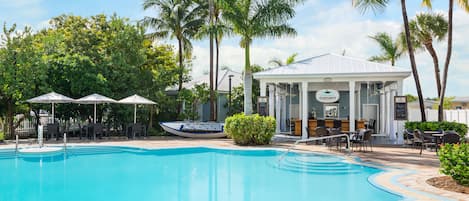 Ein Pool mit Liegestühlen und Sonnenschirmen, umgeben von Palmen und einem Gebäude mit dem Schild "Coconut".