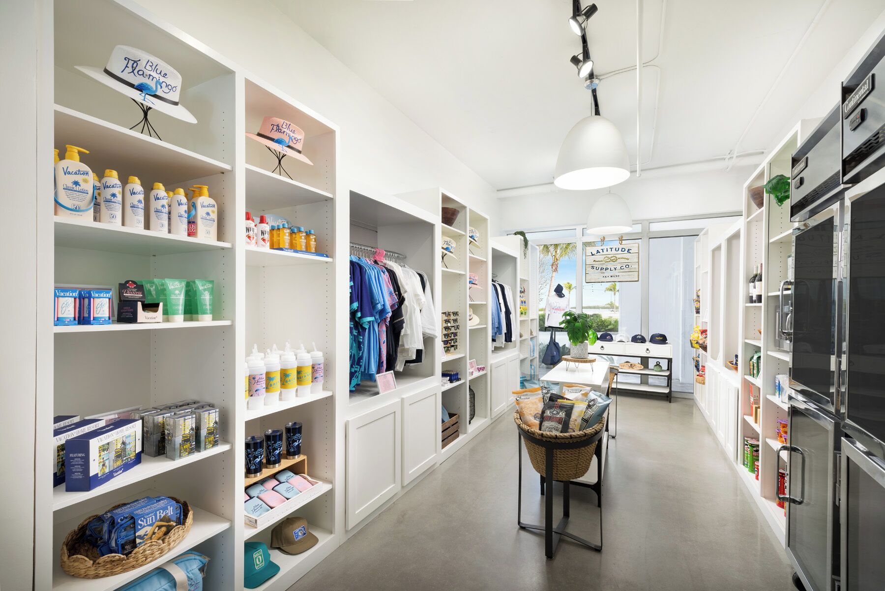 Un espace de vente bien aménagé, avec des étagères remplies de divers produits, un portant à vêtements et une table centrale sur laquelle se trouve un panier.