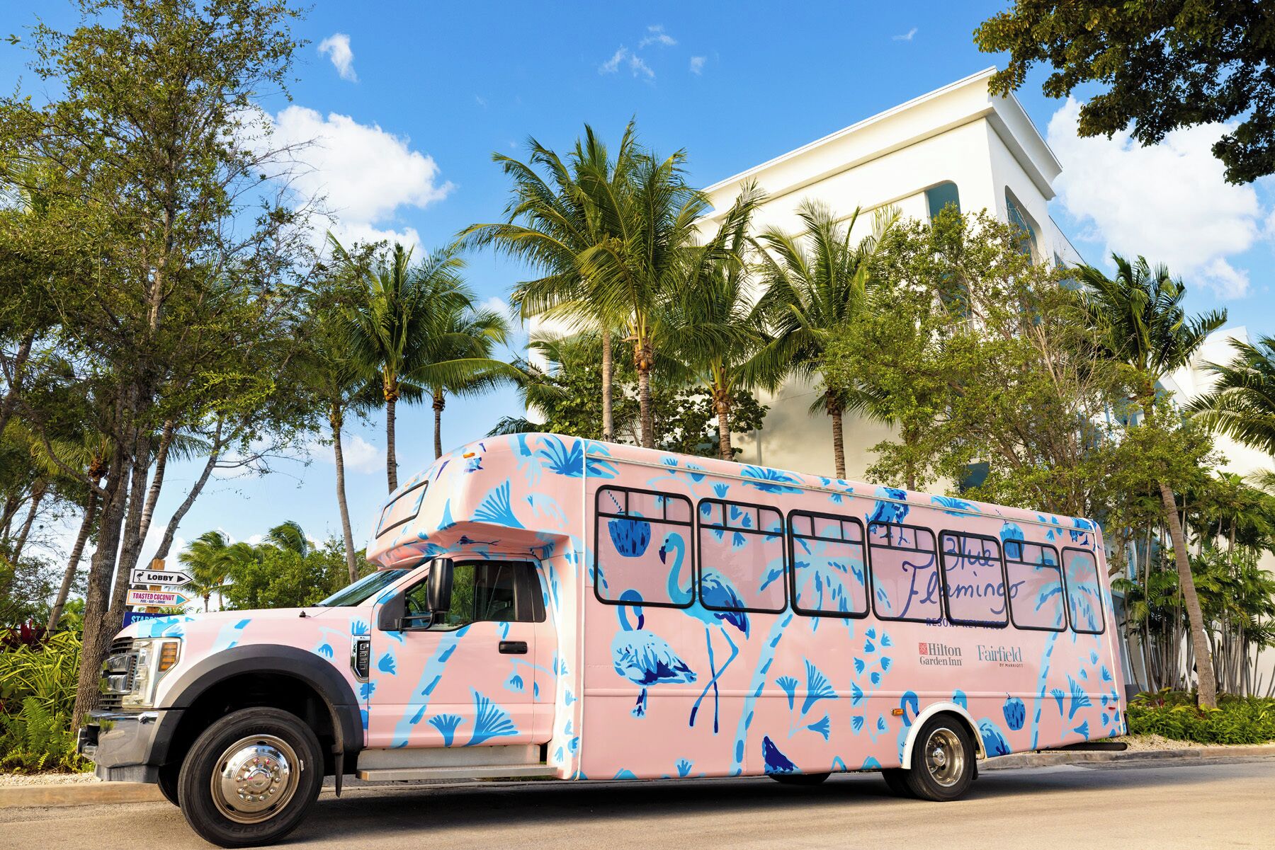A pink bus with blue tropical patterns parked on a street.