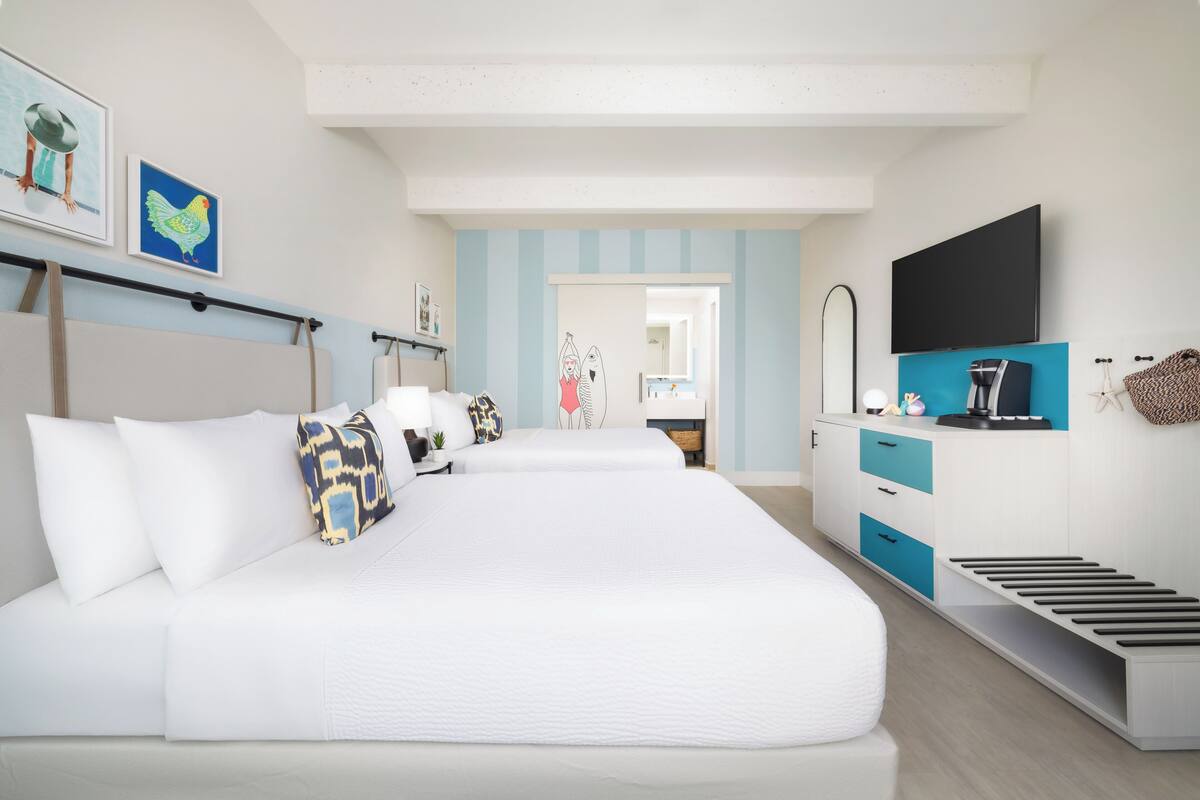 A modern hotel room with a large bed, a desk with a flat-screen TV, and a small kitchenette.