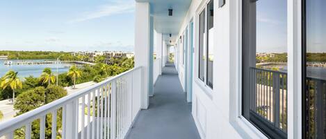 A long, narrow balcony with white railings overlooking a marina and beach.