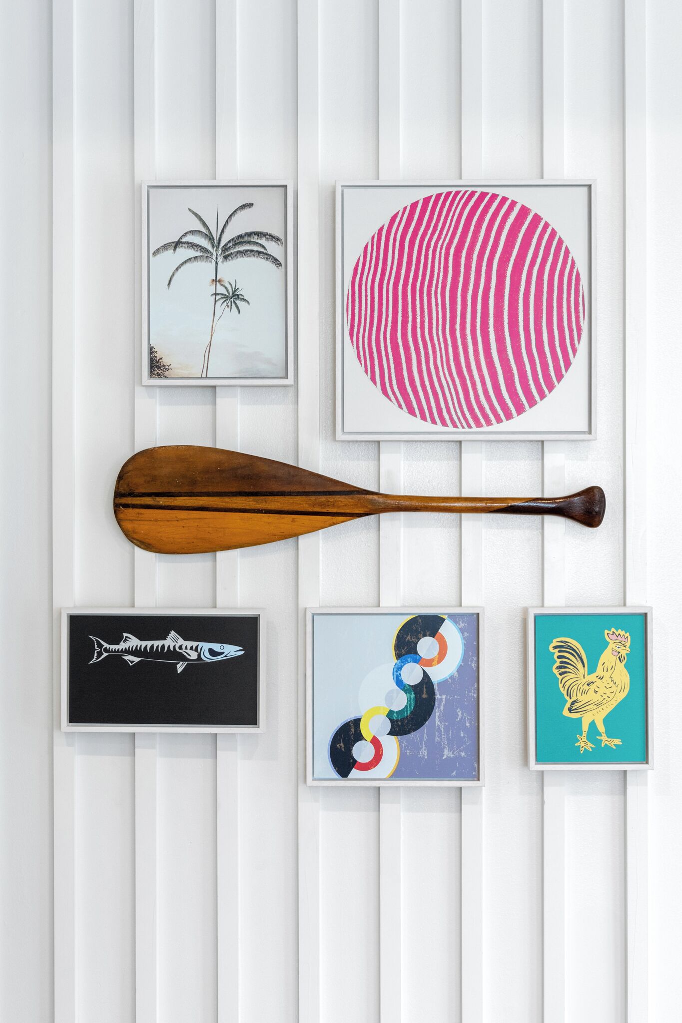 A wall with framed artwork and a wooden paddle.