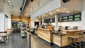 Een modern café met een houten toonbank, een zitgedeelte en schappen vol drankjes.