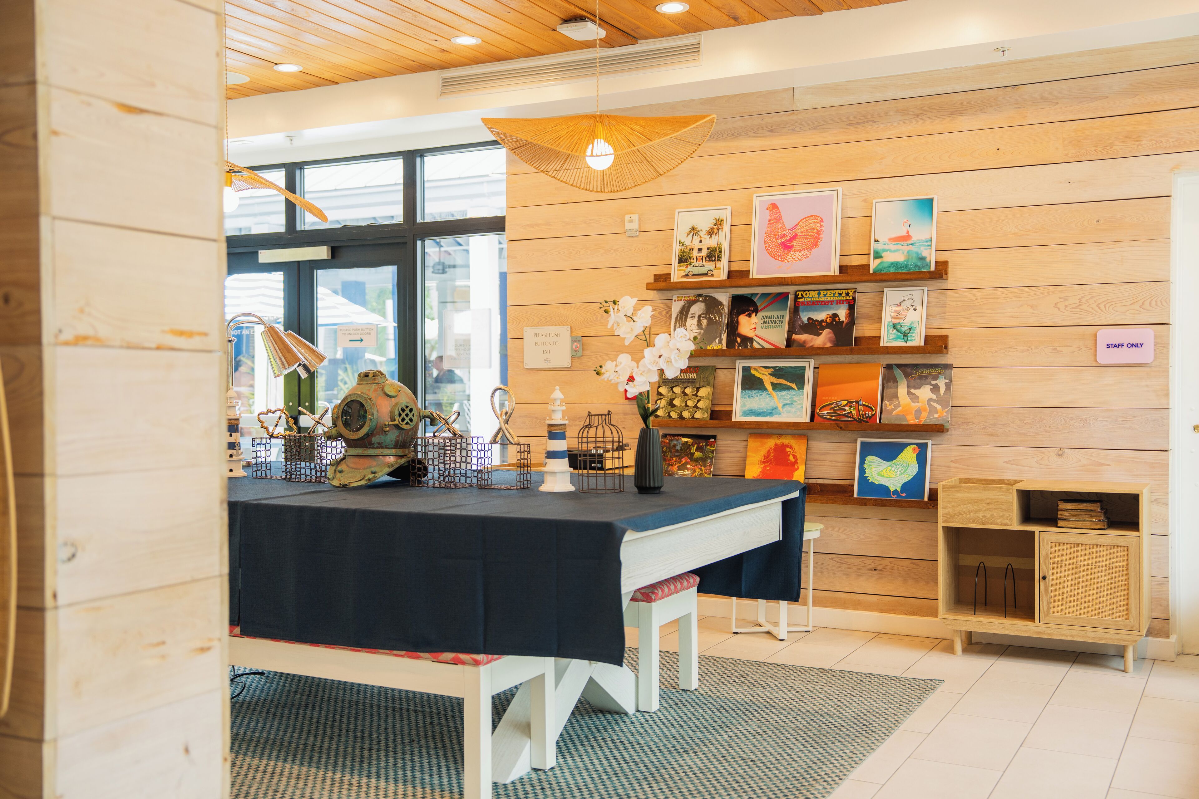A room with a wooden wall, a table with a dark tablecloth, and shelves with various items.