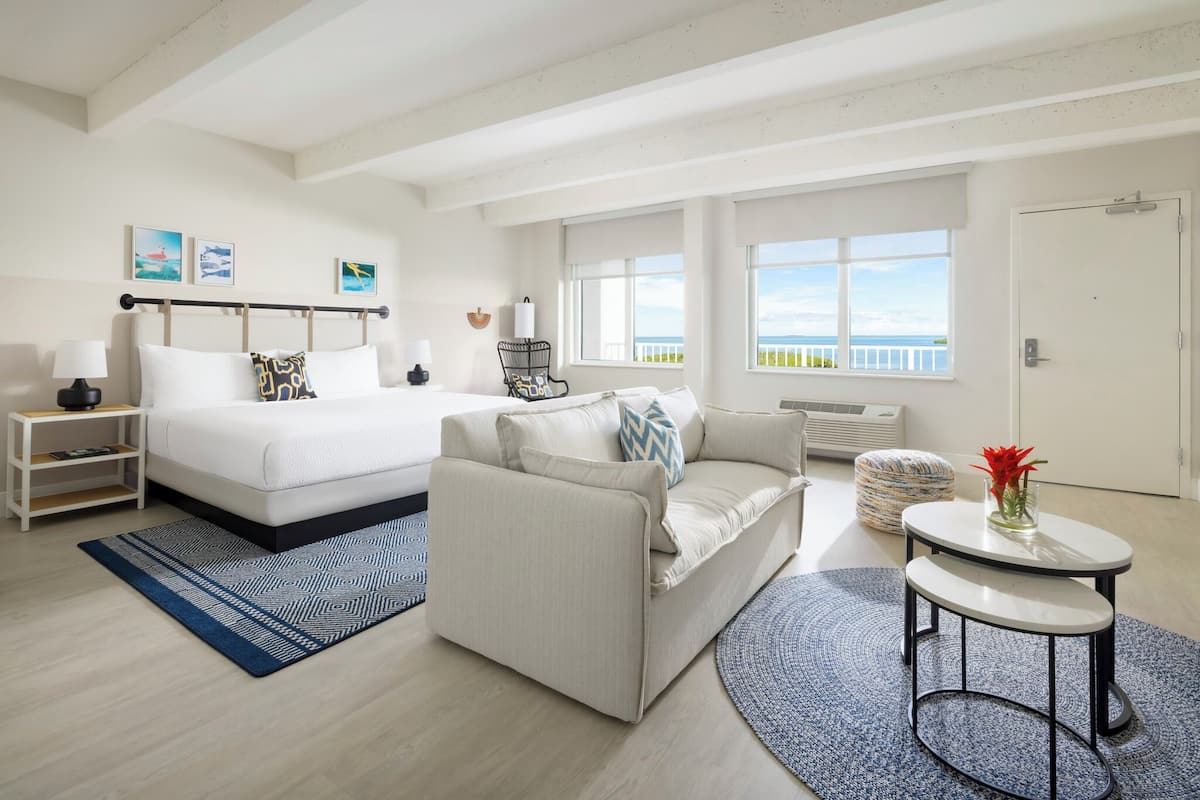 A spacious room with a bed, a sofa, a small table, and a view of the sea.