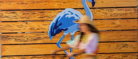 A person riding a bicycle past a wooden wall with a blue flamingo mural.
