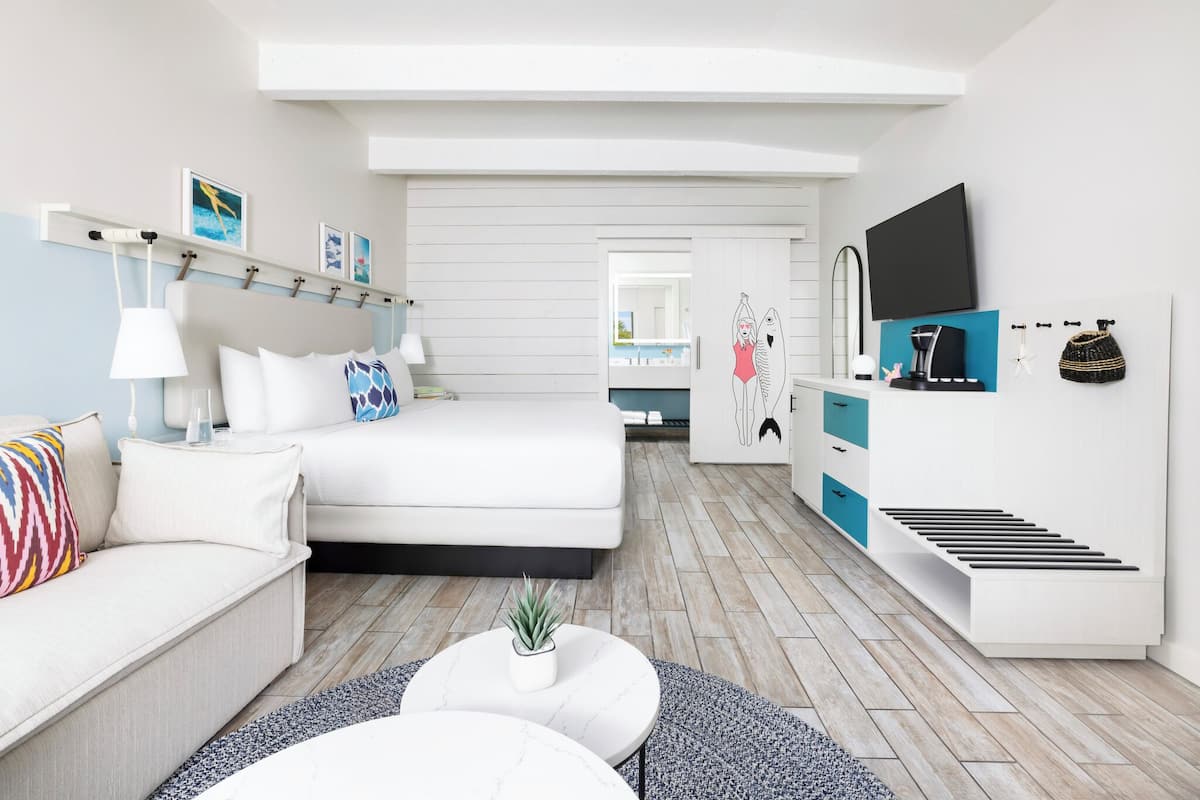 A modern hotel room with a bed, a sofa, a coffee table, a TV, and a wardrobe.