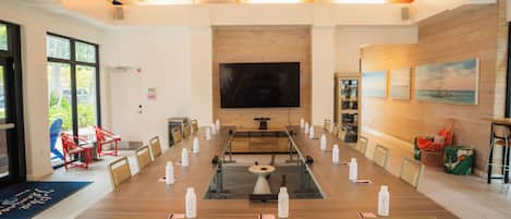 A conference room with a long table, chairs, a TV screen, and a wooden wall with paintings.