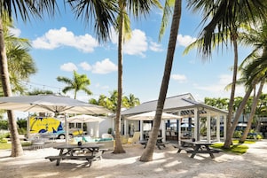 Un resort frente a la playa con palmeras, asientos al aire libre y un carrito de comida.