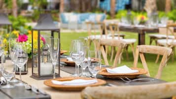 A dining table set outdoors with wicker chairs, clear glassware, and a candle centerpiece.