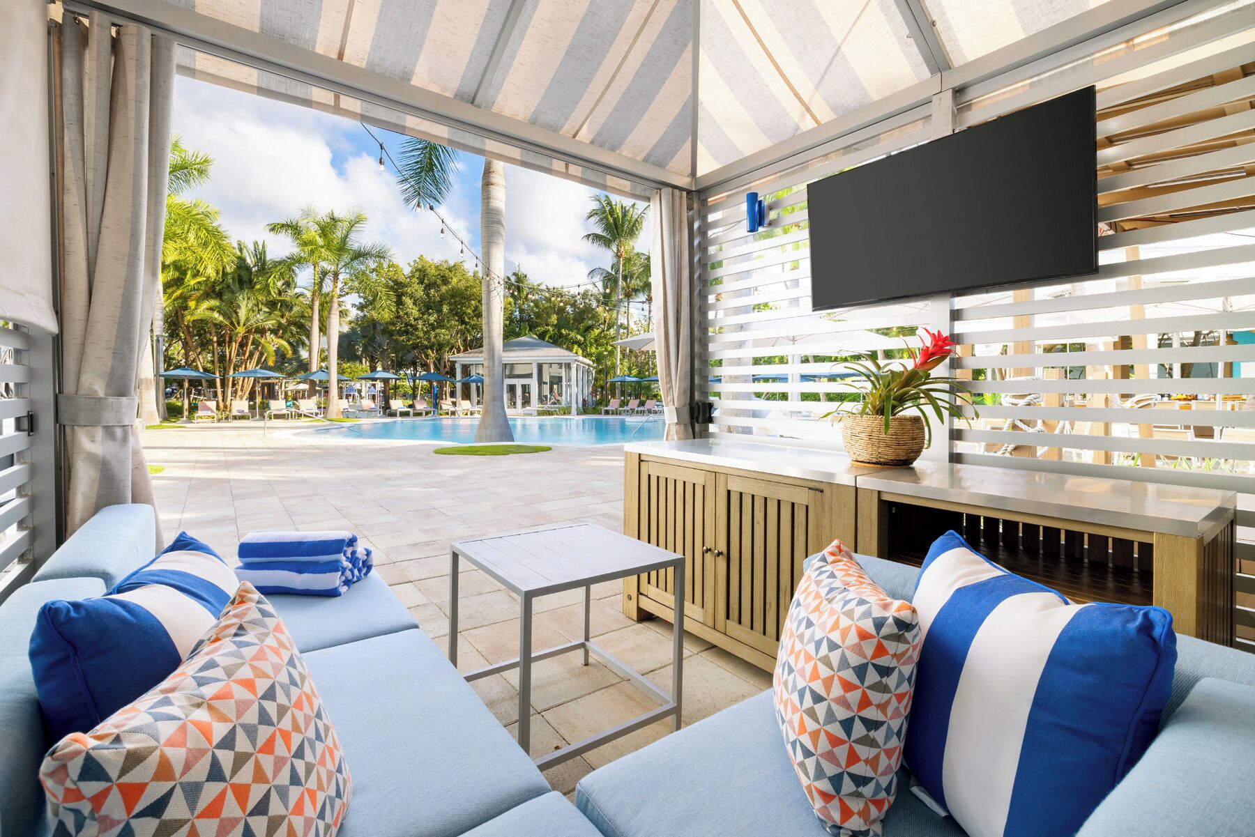 Un espace de détente extérieur moderne, avec vue sur la piscine, un téléviseur à écran plat et un meuble en bois.