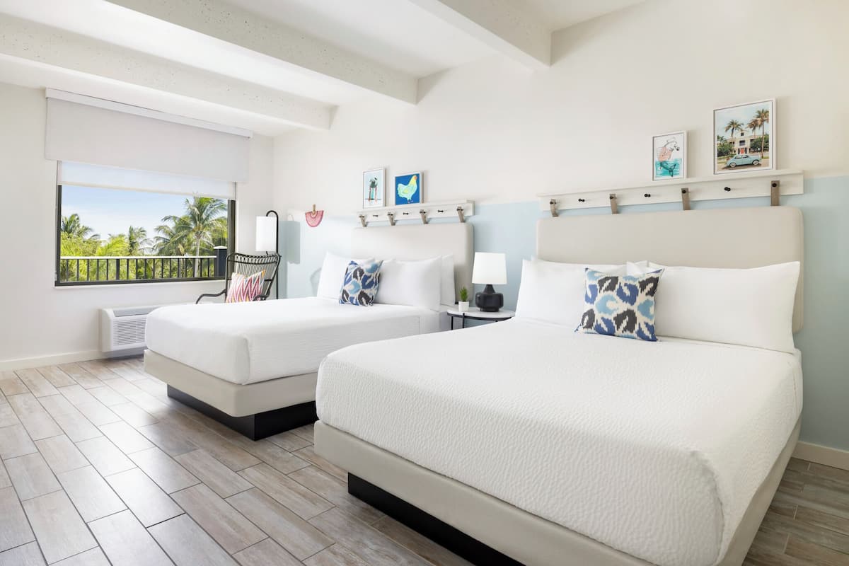 A hotel room with two beds, a balcony with a view of palm trees, and a ceiling with exposed beams.