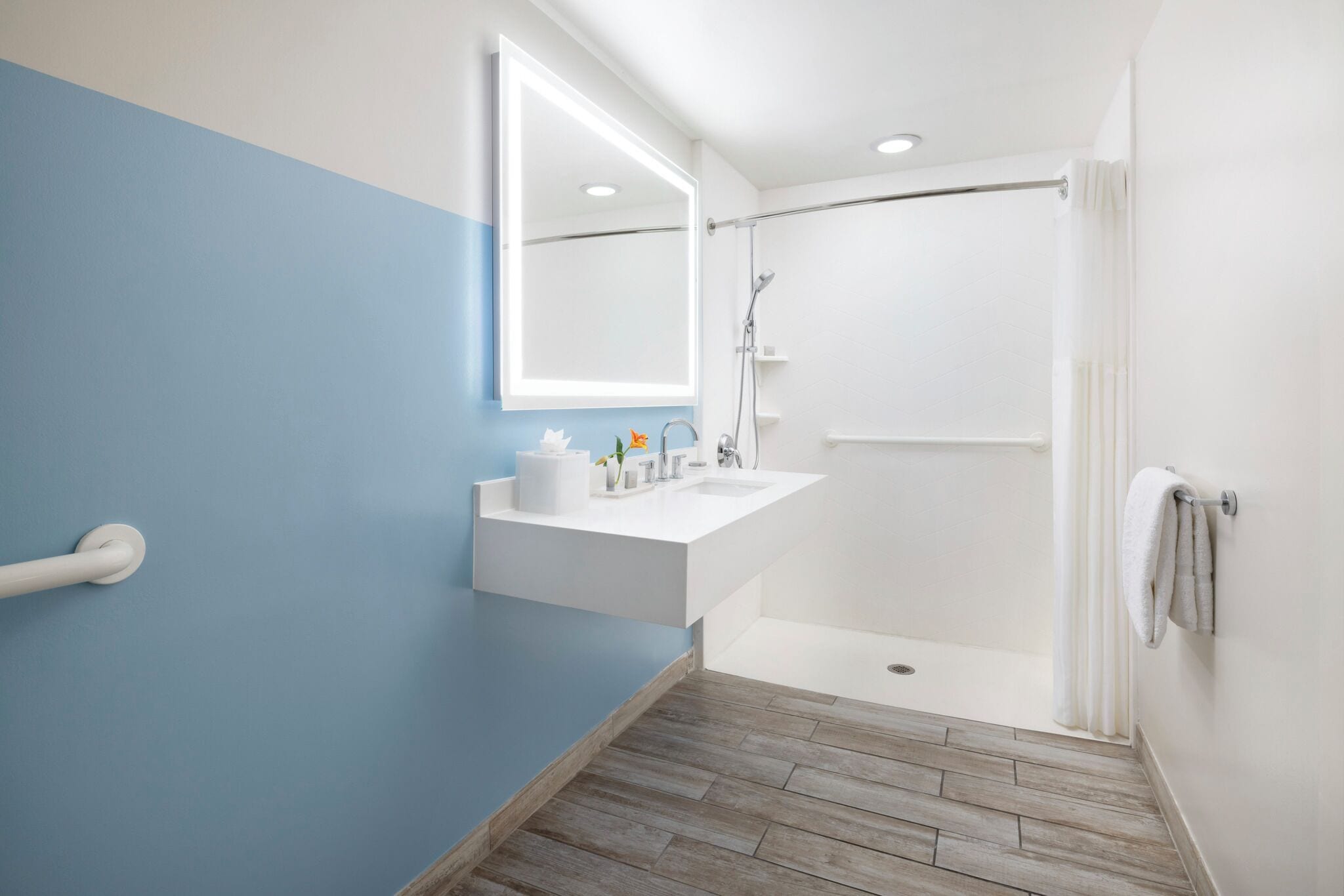 Un baño con una decoración azul y blanca, un lavabo blanco, un espejo, una ducha y suelo de madera.
