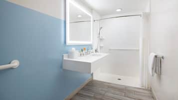 Un baño con una decoración azul y blanca, un lavabo blanco, un espejo, una ducha y suelo de madera.