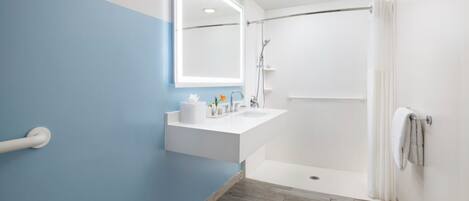 Une salle de bain aux couleurs bleu et blanc, avec un lavabo blanc, un miroir, une douche et un plancher en bois.