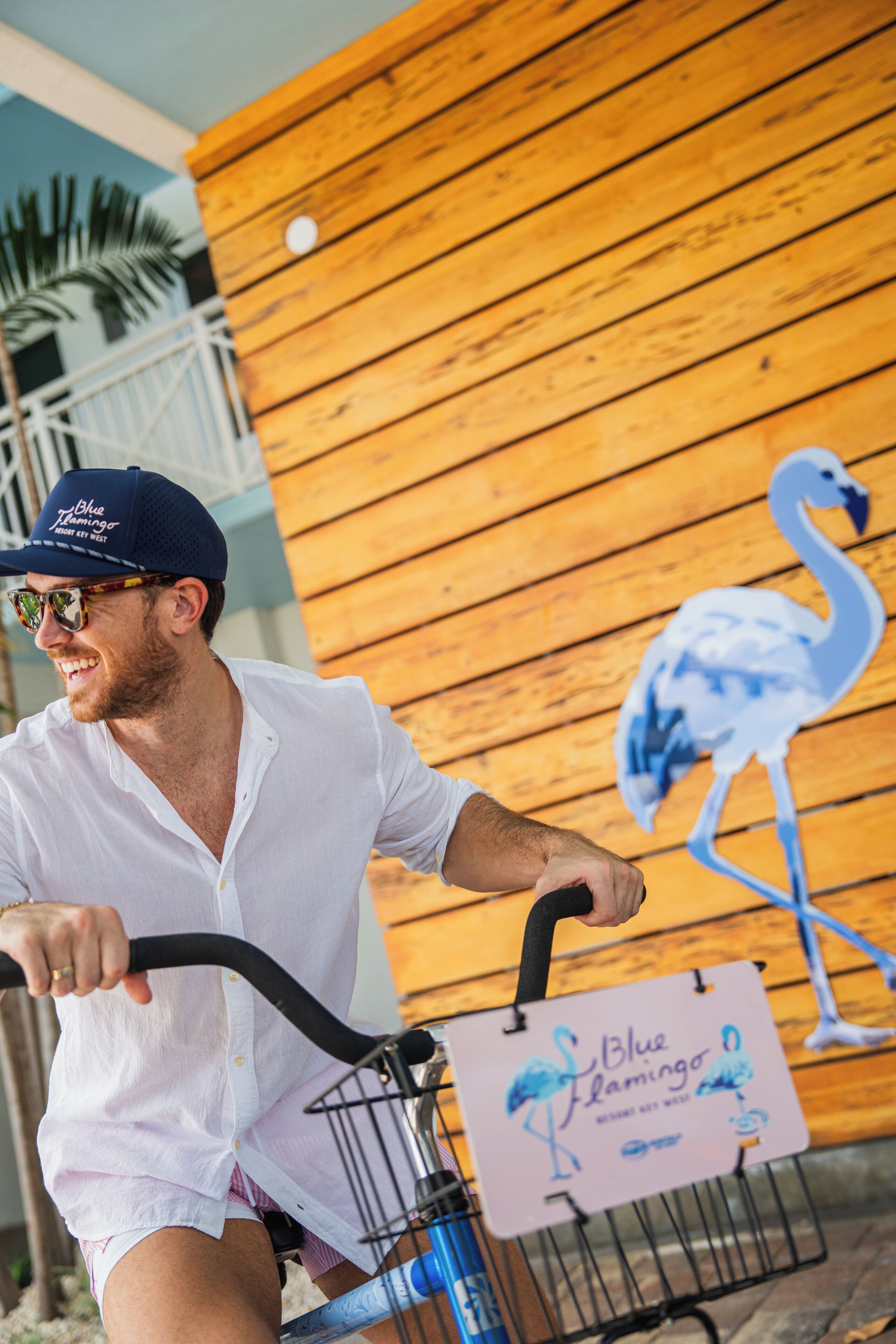 A person riding a bicycle with a sign that reads "Blue Flamingo" and a wooden wall with a flamingo mural.