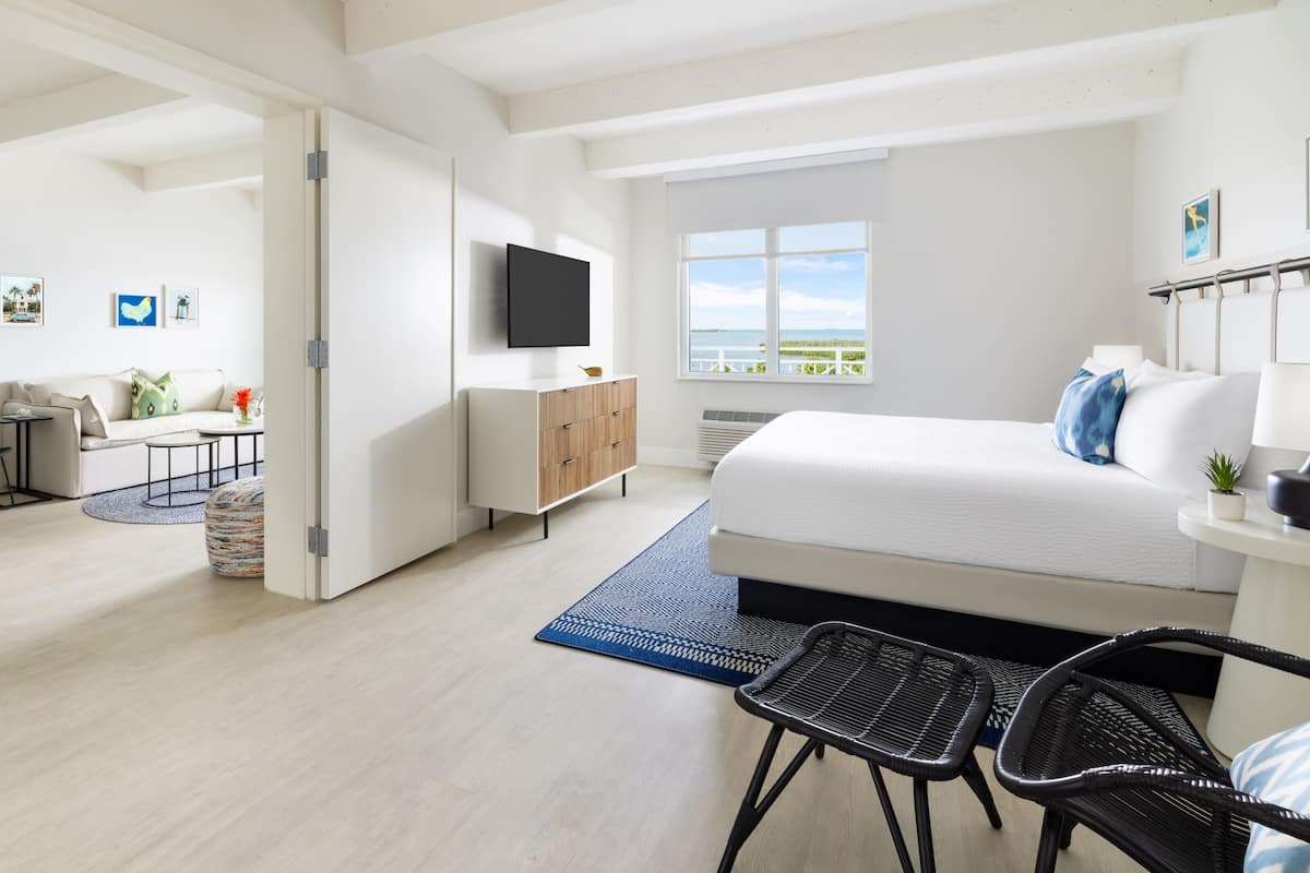 A modern hotel room with a large bed, a TV, a desk, and a view of the outdoors.