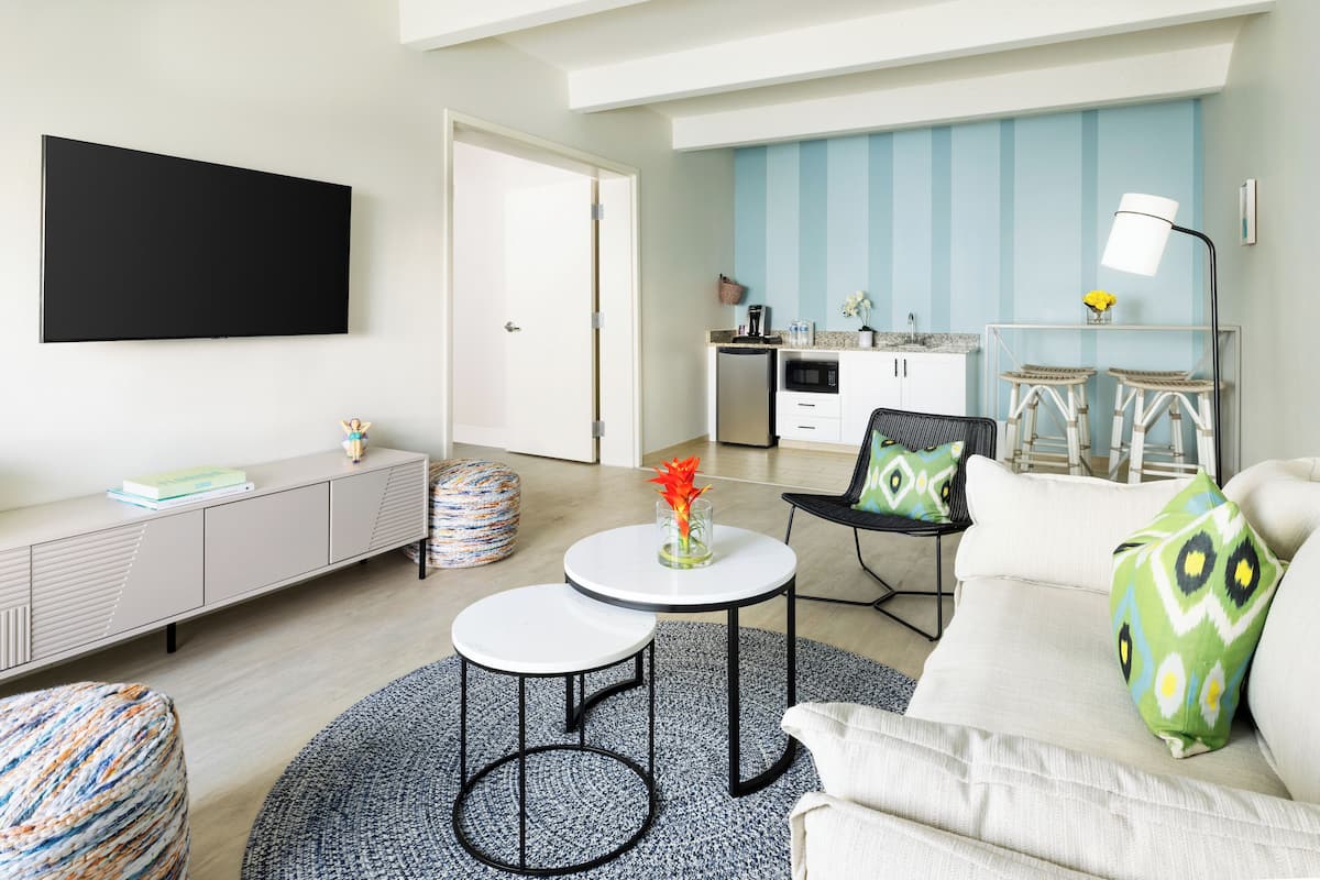 A modern living room with a sofa, two round tables, a TV, and a kitchen in the background.
