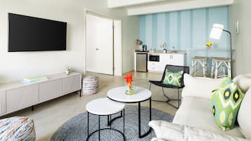 A modern living room with a sofa, two round tables, a TV, and a kitchen in the background.