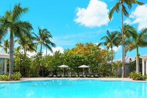 A swimming pool with lounge chairs and umbrellas, surrounded by palm trees and greenery. - Blue Flamingo Resort Key West (Key West)