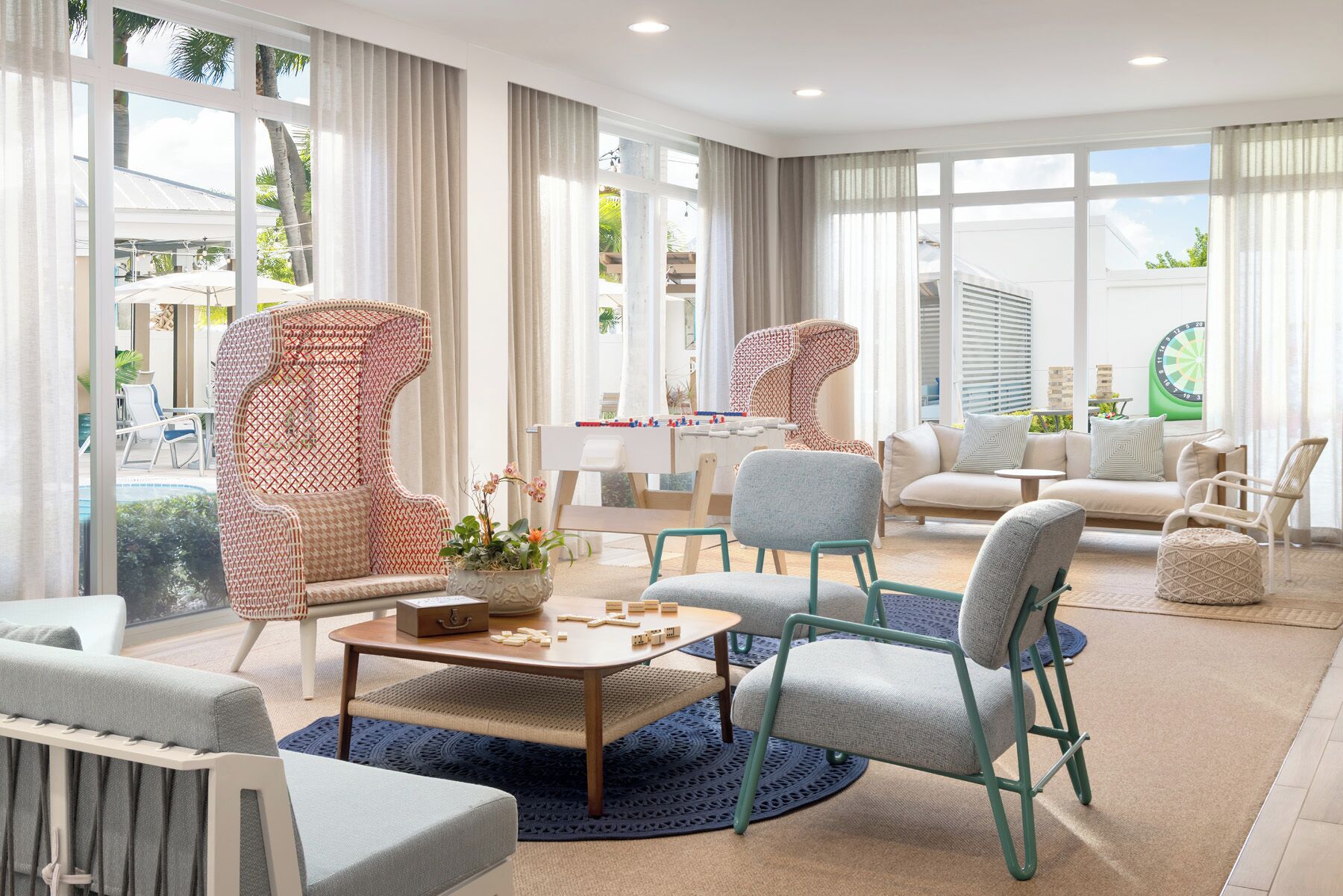 Un amplio salón con mesa de fútbol de mesa, asientos cómodos y ventanas grandes con vistas al exterior.
