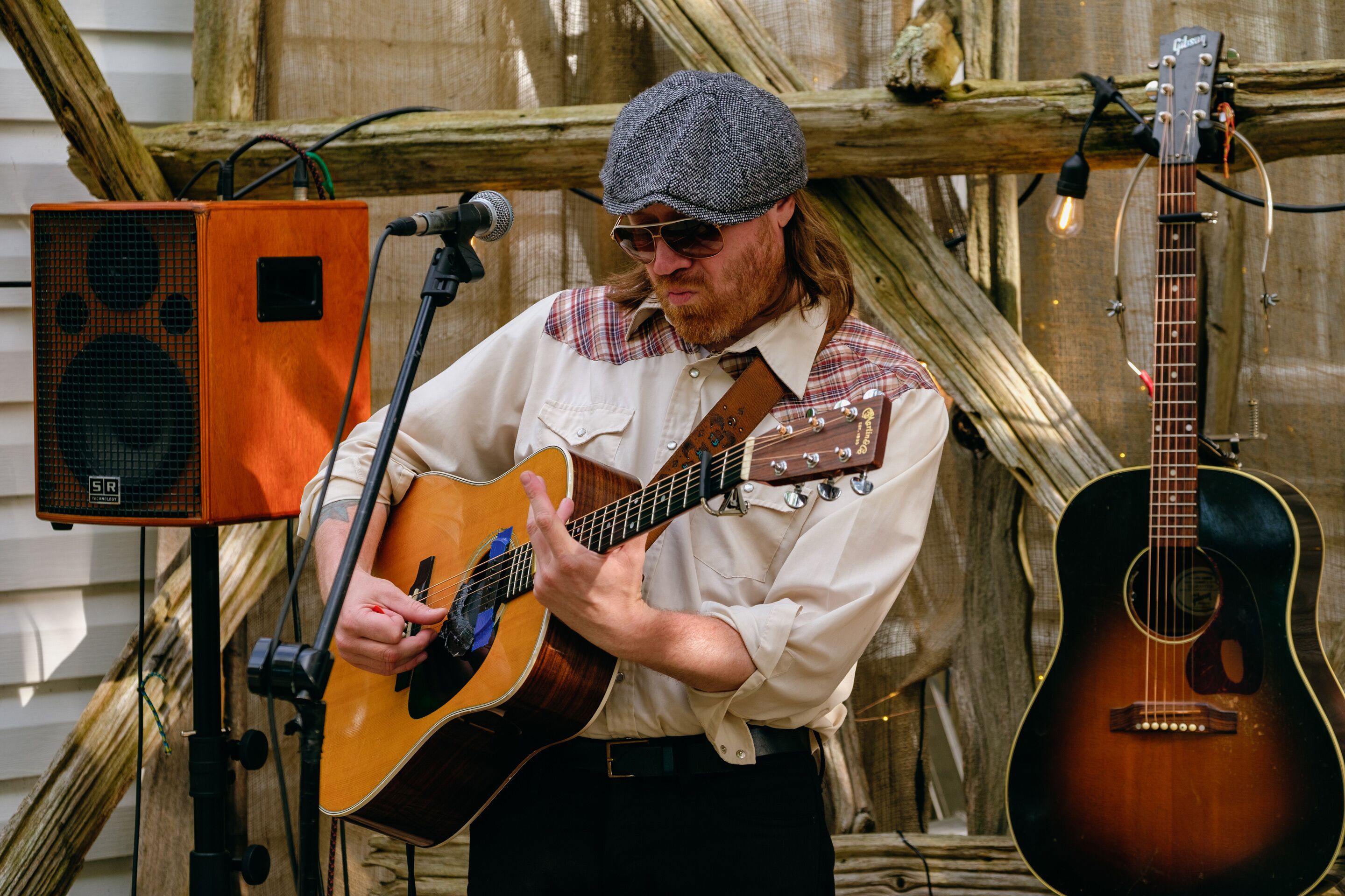 A person playing an acoustic guitar with a microphone stand and amplifier in a rustic setting.