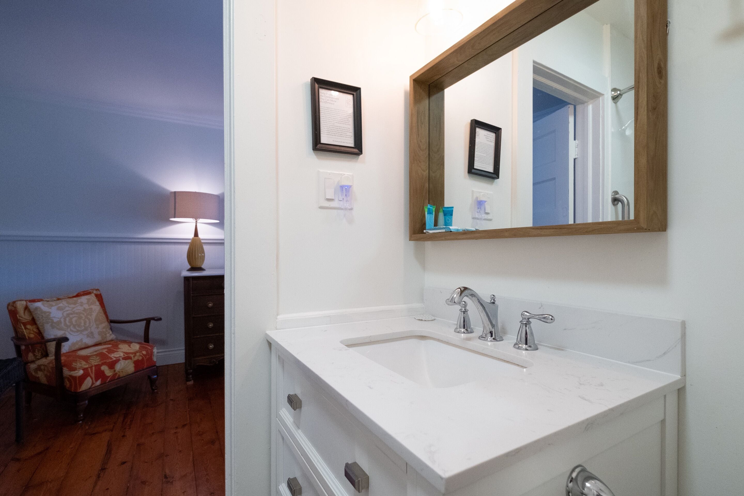 A bathroom with a white sink, a large mirror, and a wooden chair.