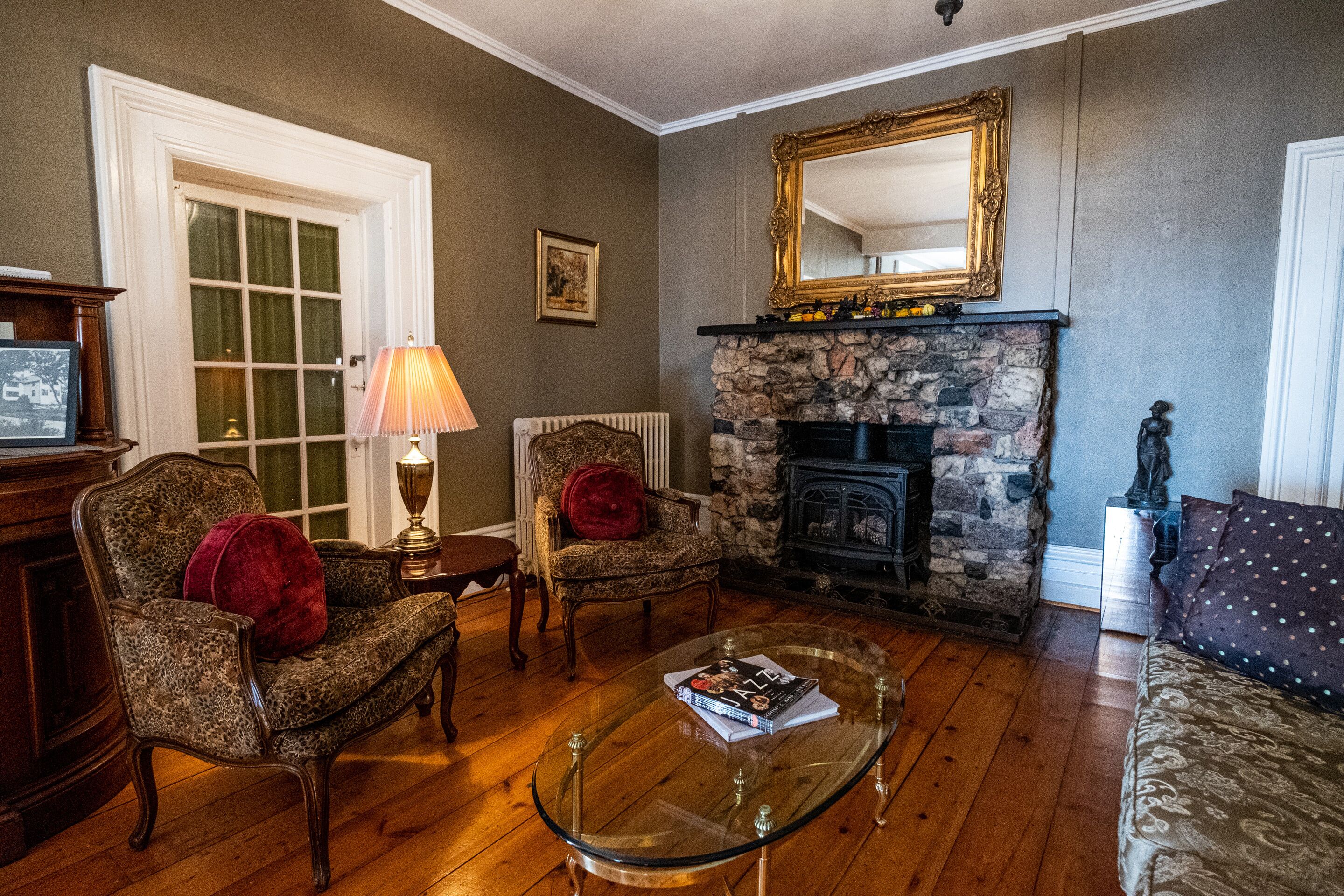 A living room with a fireplace, a glass coffee table, two armchairs, a sofa, and a large mirror on the wall.