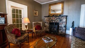 A living room with a fireplace, a glass coffee table, two armchairs, a sofa, and a large mirror on the wall.