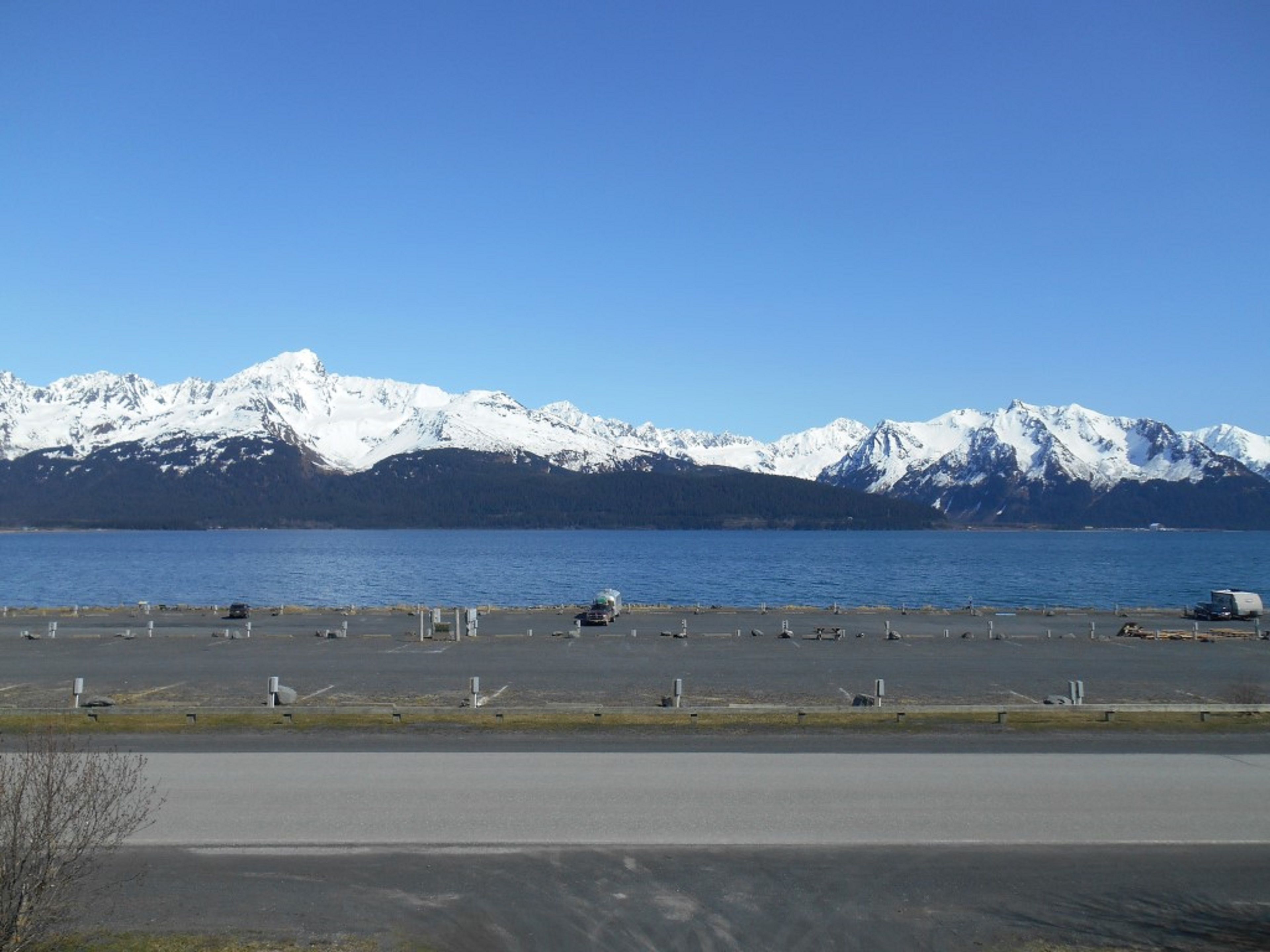 A parking area with vehicles and a view of snow-capped mountains in the background.