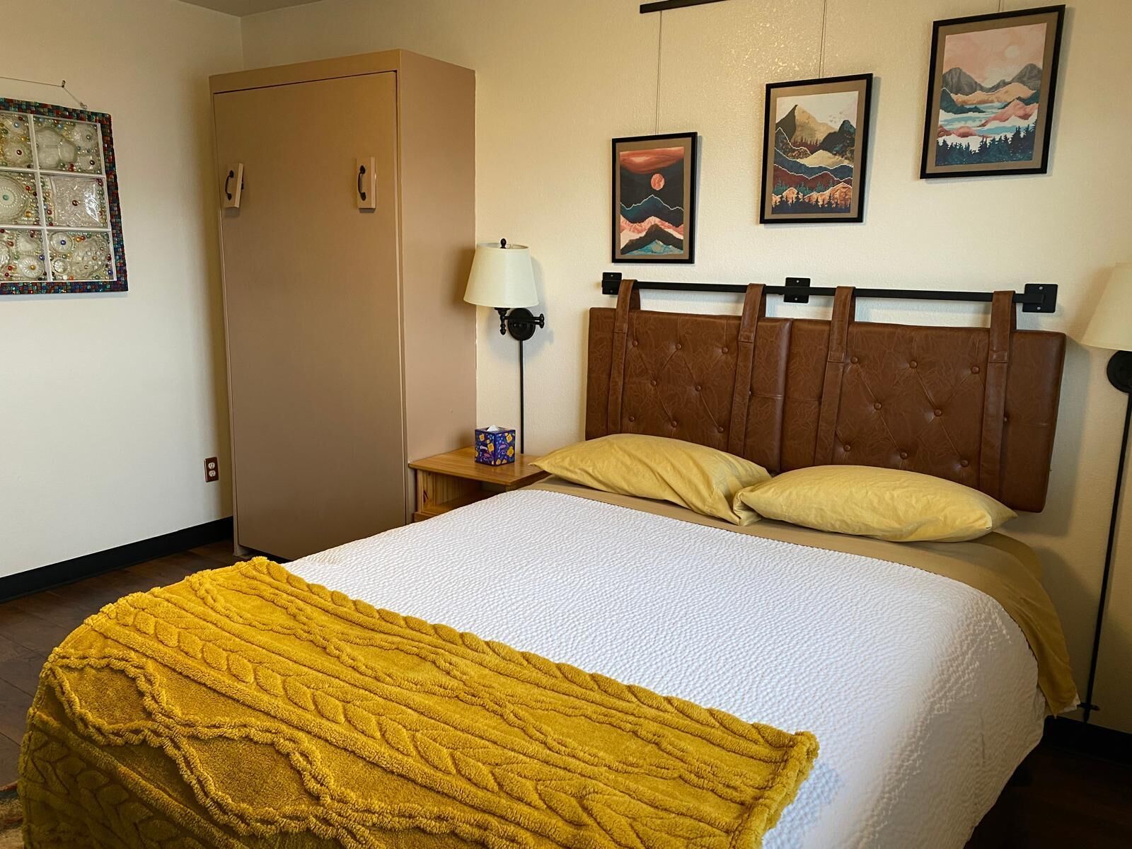 Ein Hotelzimmer mit Bett, Kleiderschrank, Nachttisch mit Lampe und Wandbild.