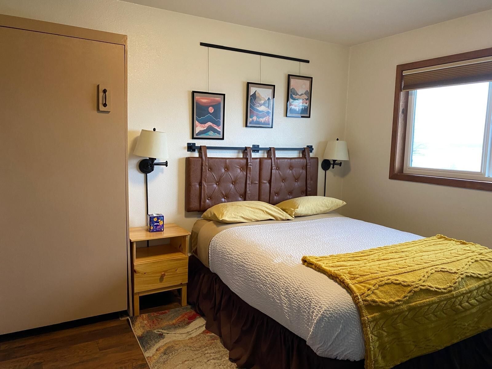 A neatly arranged bedroom with a bed, bedside lamps, a nightstand, a wardrobe, and framed artwork on the wall.