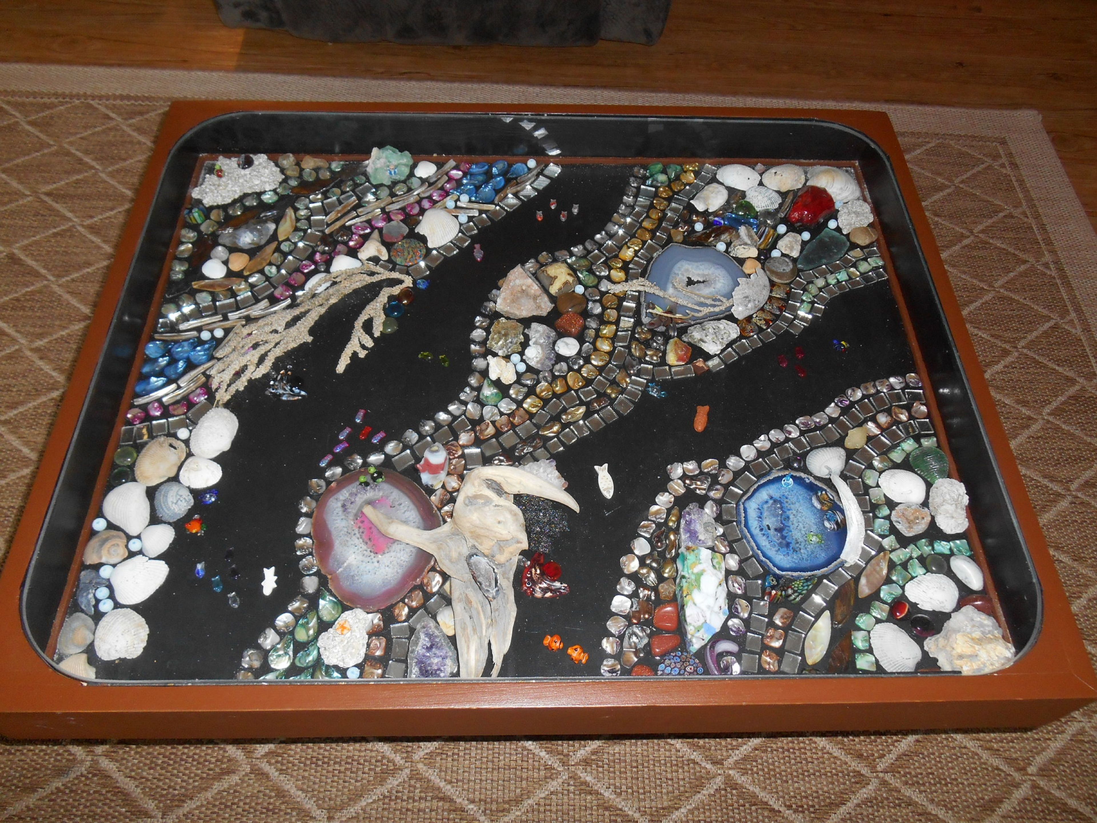 Une table carrée ornée d’une mosaïque composée de différents types de pierres et de coquillages.