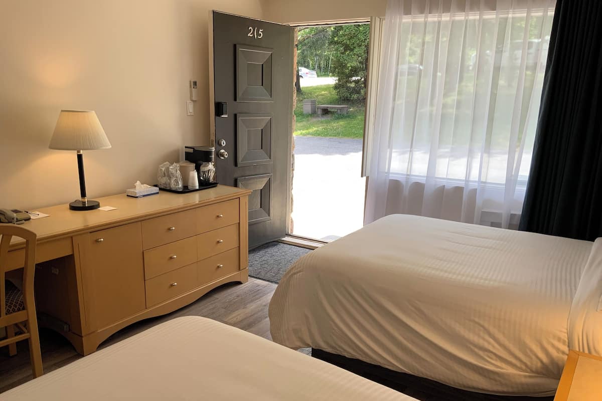 A hotel room with two beds, a desk with a lamp, a dresser, and a door marked "215".
