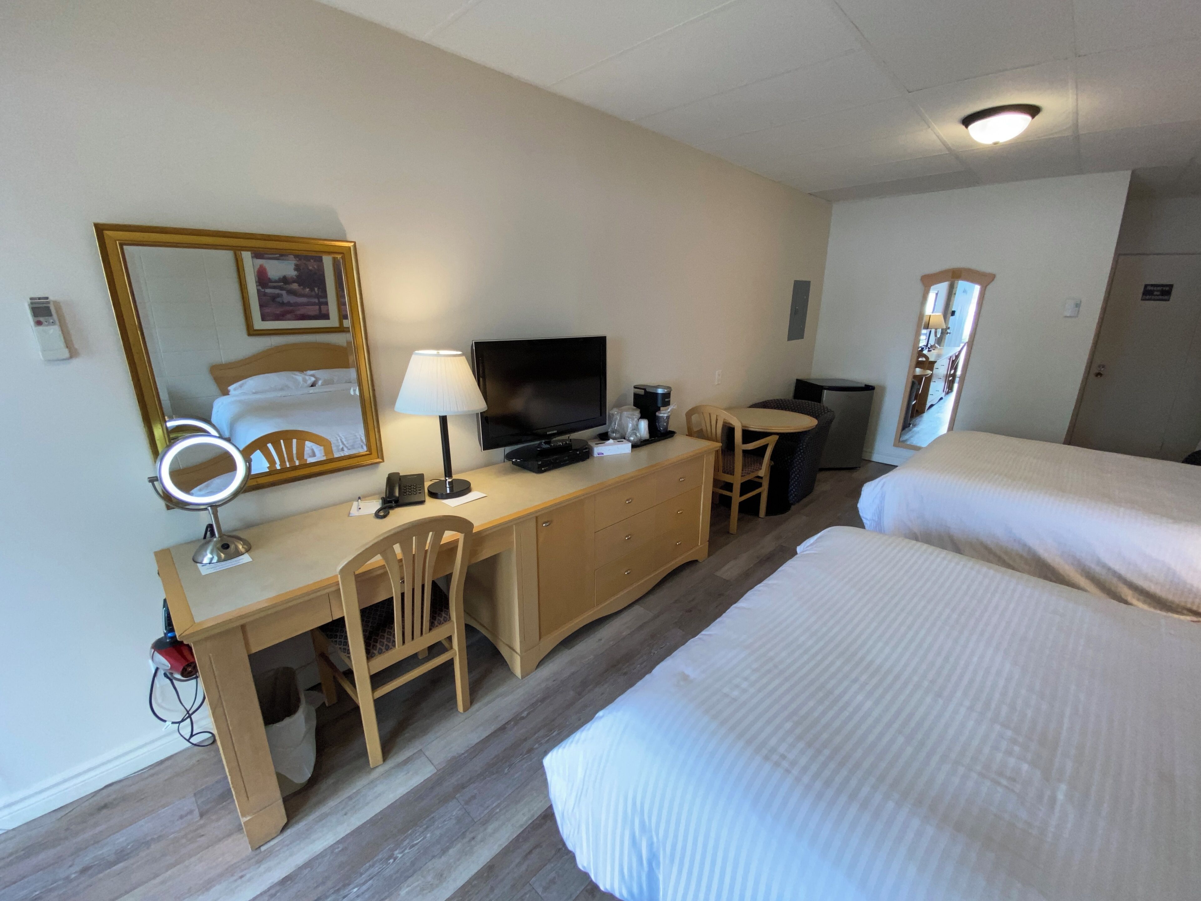 A hotel room with a bed, a desk with a computer, a chair, a television, and a mirror.