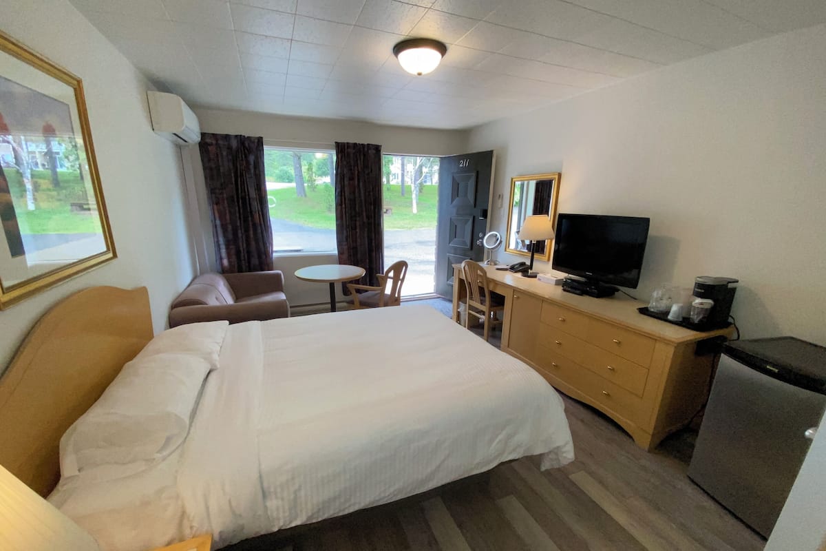 A hotel room with a bed, a desk with a television, a chair, a small table, and a mirror.