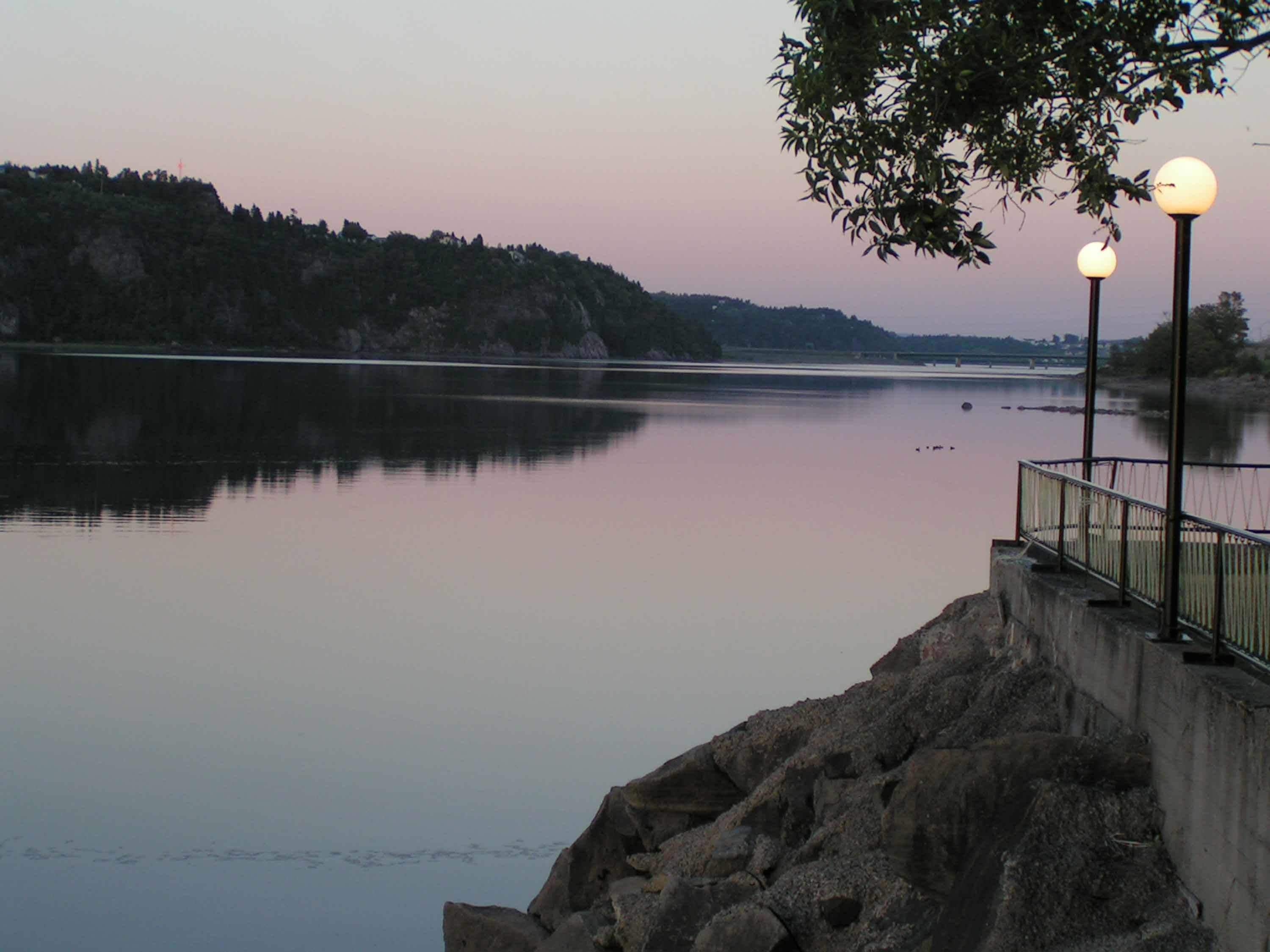 A calm river with a rocky embankment and a metal railing.