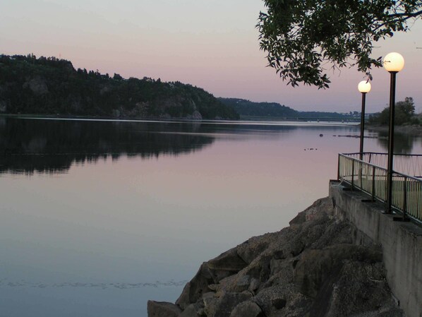 A calm river with a rocky embankment and a metal railing. - Motel Panoramique (Saguenay)