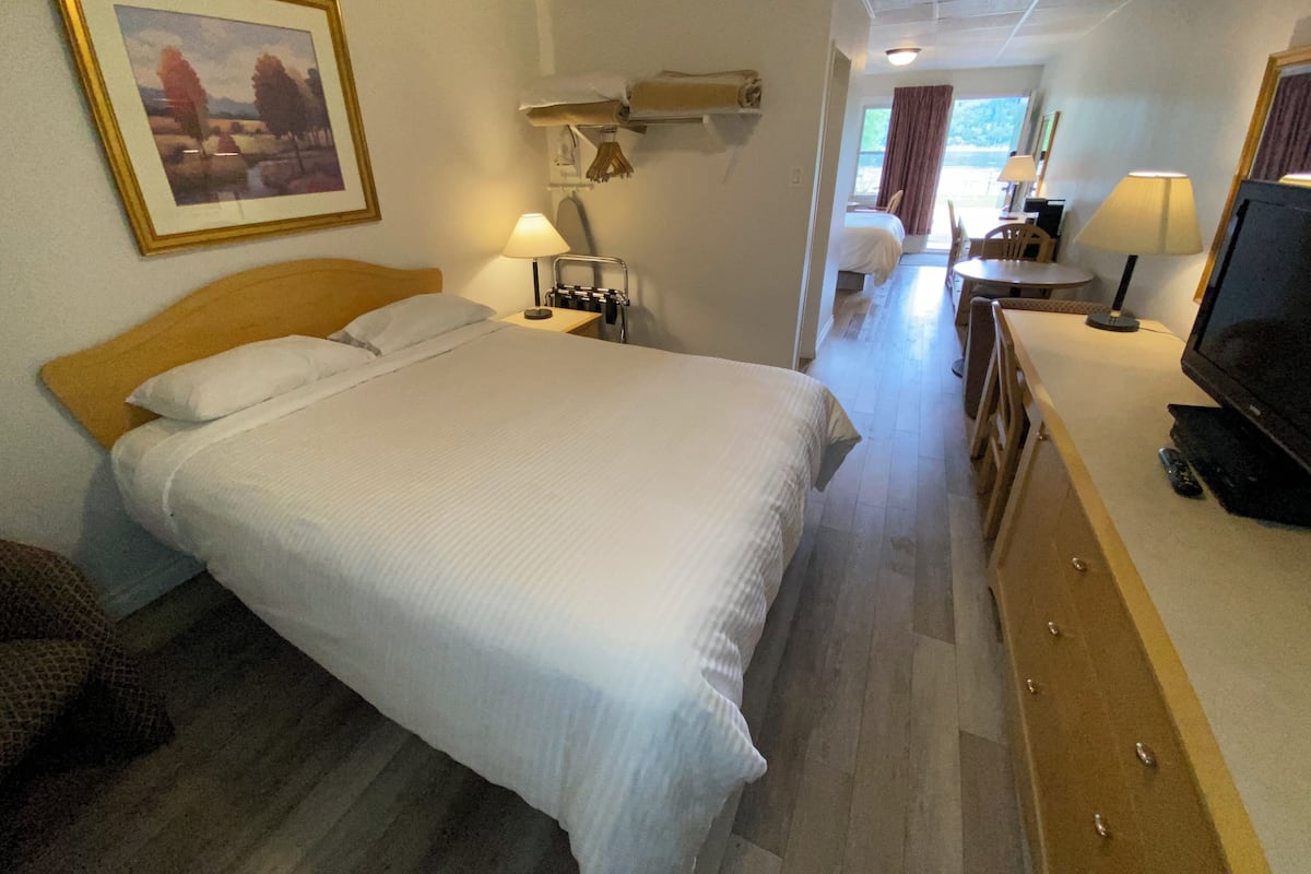 A hotel room with a large bed, bedside tables, a TV, and a desk with a chair.